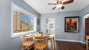 A dining area with a table set for four, a ceiling fan, and a large window with a view of a backyard.