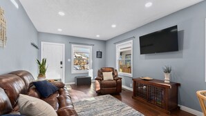 A living room with a leather couch, a brown leather chair, a wooden console table, and a flat-screen TV mounted on the wall.