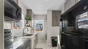 A compact kitchen with a black refrigerator, stainless steel appliances, and a window providing a view of the outside.