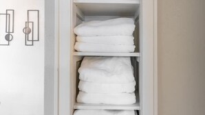 Um armário branco com várias prateleiras e uma gaveta, contendo toalhas brancas dobradas com capricho.