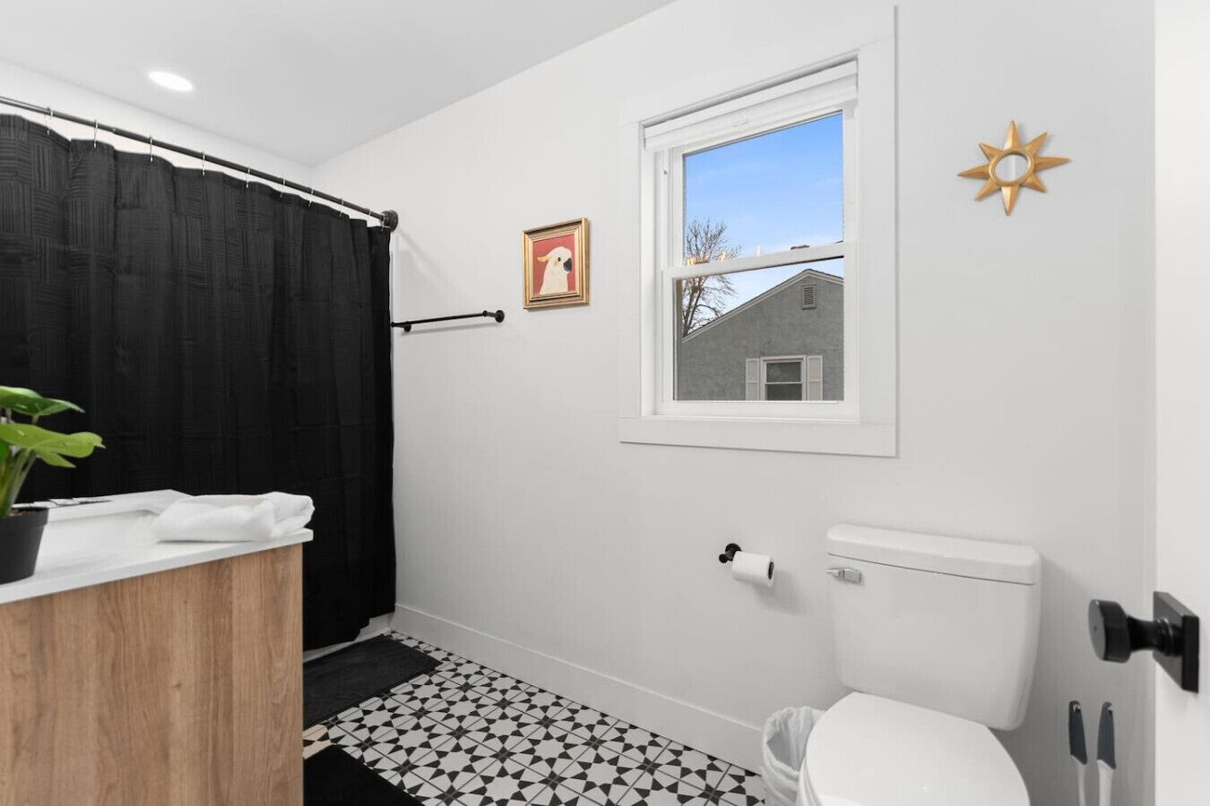 A bathroom with a toilet, a shower curtain, a window, and a small framed picture on the wall.