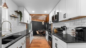 Een moderne keuken met witte kasten, zwarte aanrechtbladen en een houten trap op de achtergrond.