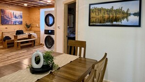 A dining area with a wooden table, chairs, a bench, and a washing machine in the background.