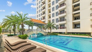 A swimming pool with lounge chairs, palm trees, and a building with balconies. - Tensia by Kozystay - Taman Sari (Jakarta)