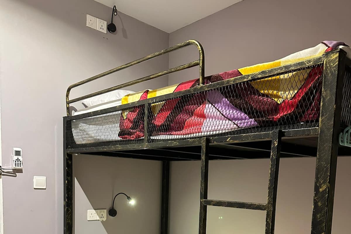 A bunk bed with a colorful quilt, a white pillow, and a wall-mounted light.