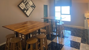 Een eethoek met een houten tafel en barstoelen, een plafondventilator en een raam met jaloezieën.