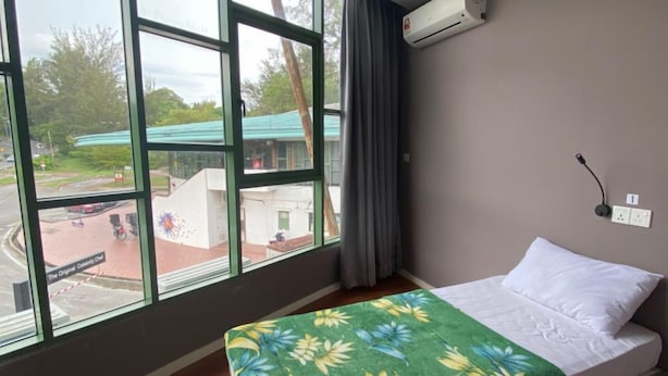 Hotelkamer met groot raam, bed met bloemenbedekking, wandairconditioning en uitzicht op straat en groen.