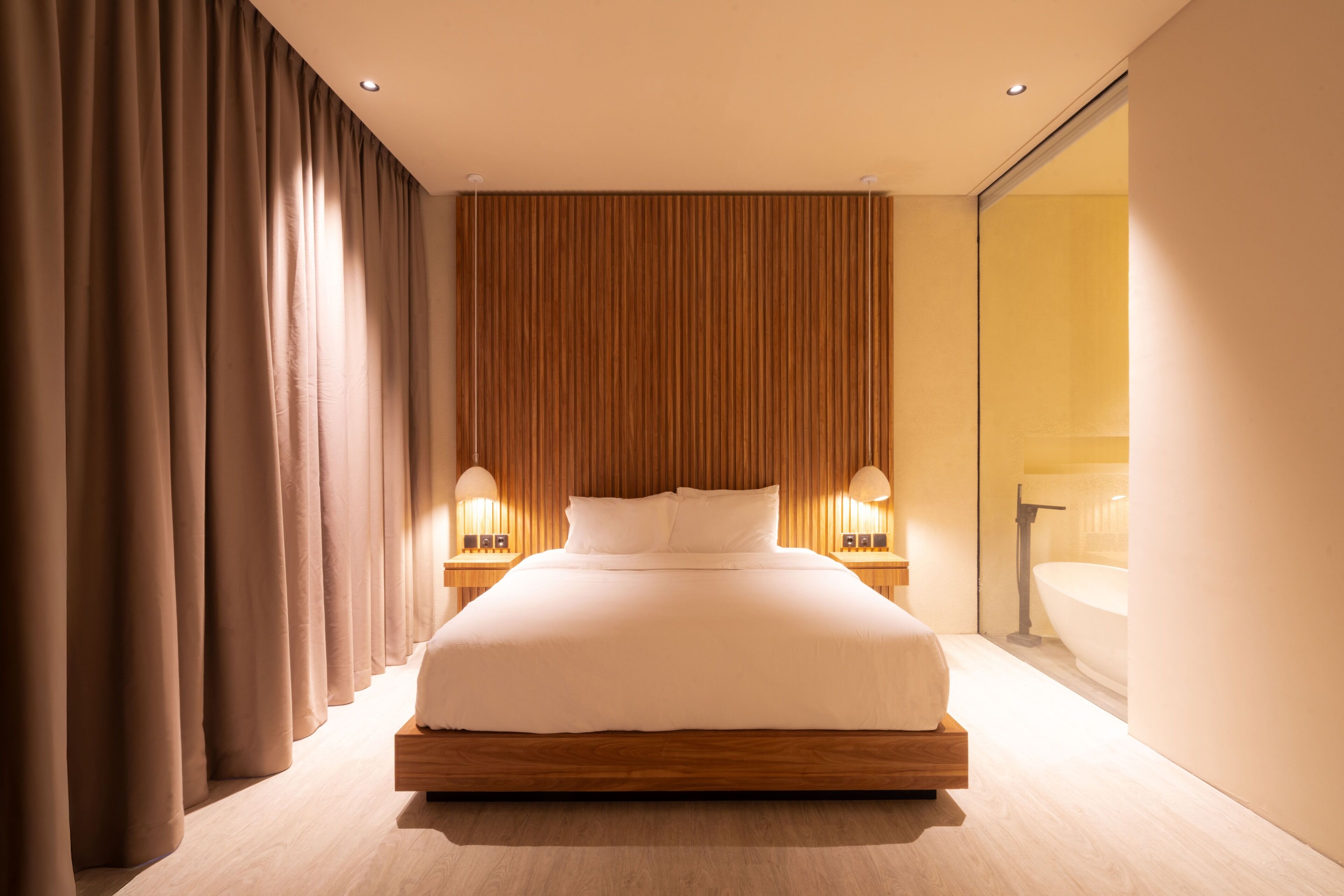 Une chambre d’hôtel moderne avec un grand lit, une tête de lit en bois et des lampes de chevet.