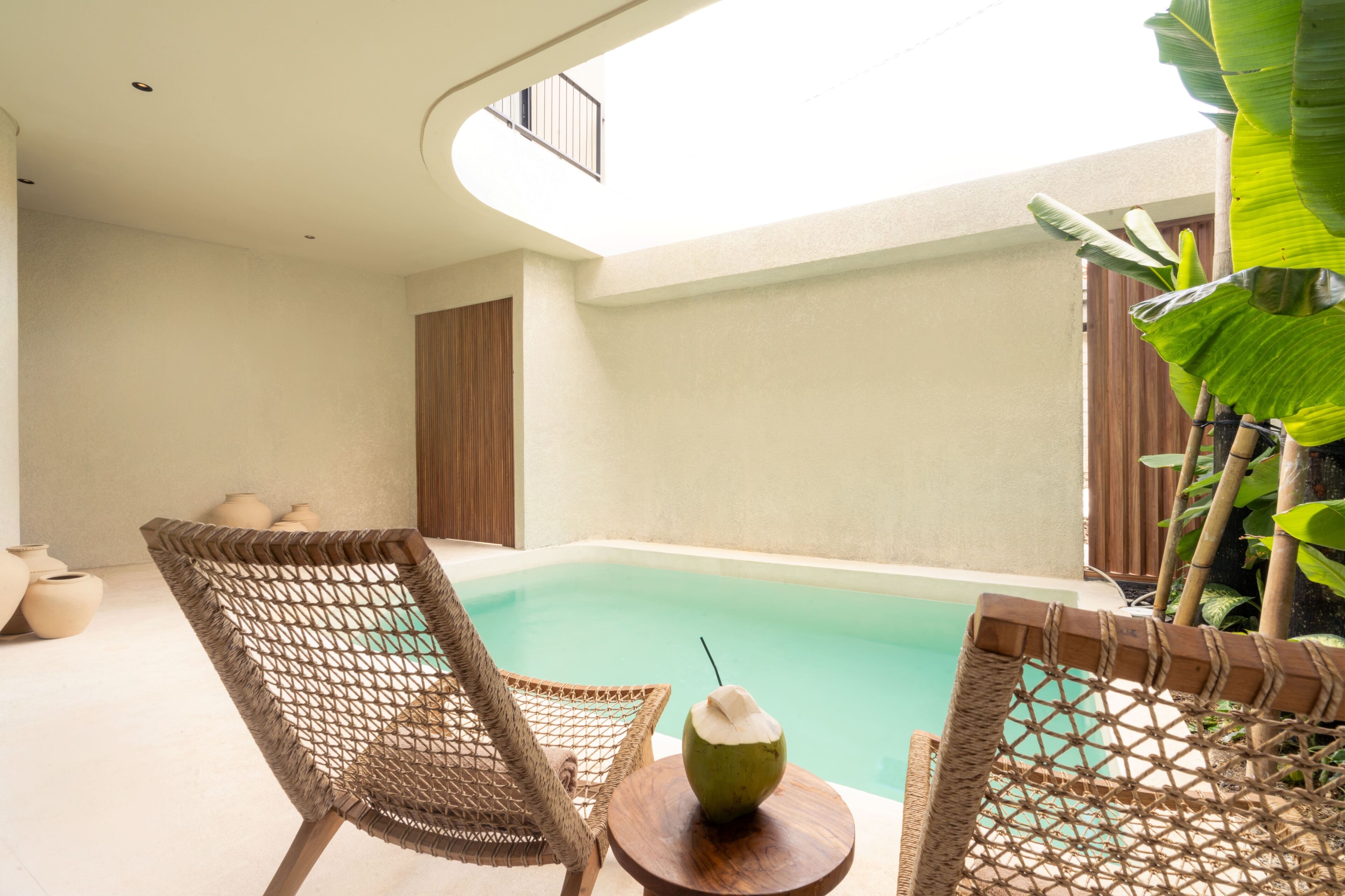 Un espace aménagé au bord de la piscine, avec des fauteuils en osier, une petite table ronde sur laquelle est posée une boisson à la noix de coco, et une vue sur la piscine.