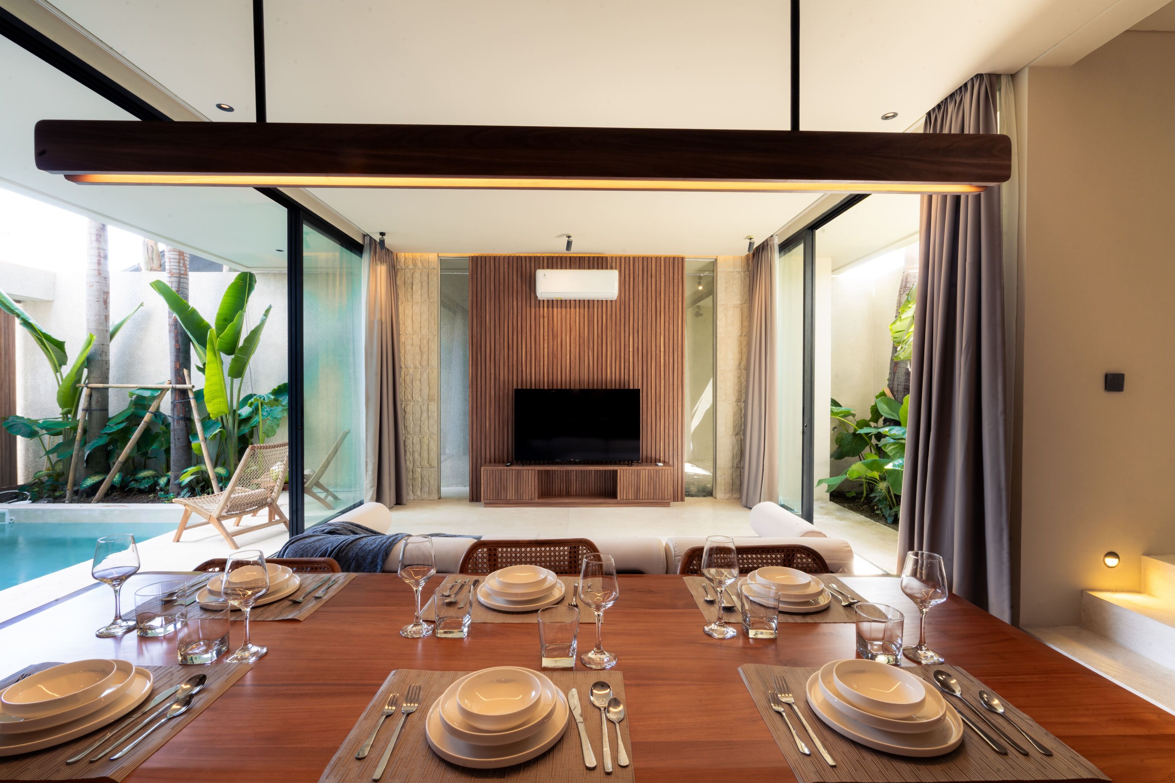 Un espace repas moderne avec vue sur la piscine, un téléviseur à écran plat et un coin salon agrémenté d’un mur en panneaux de bois.