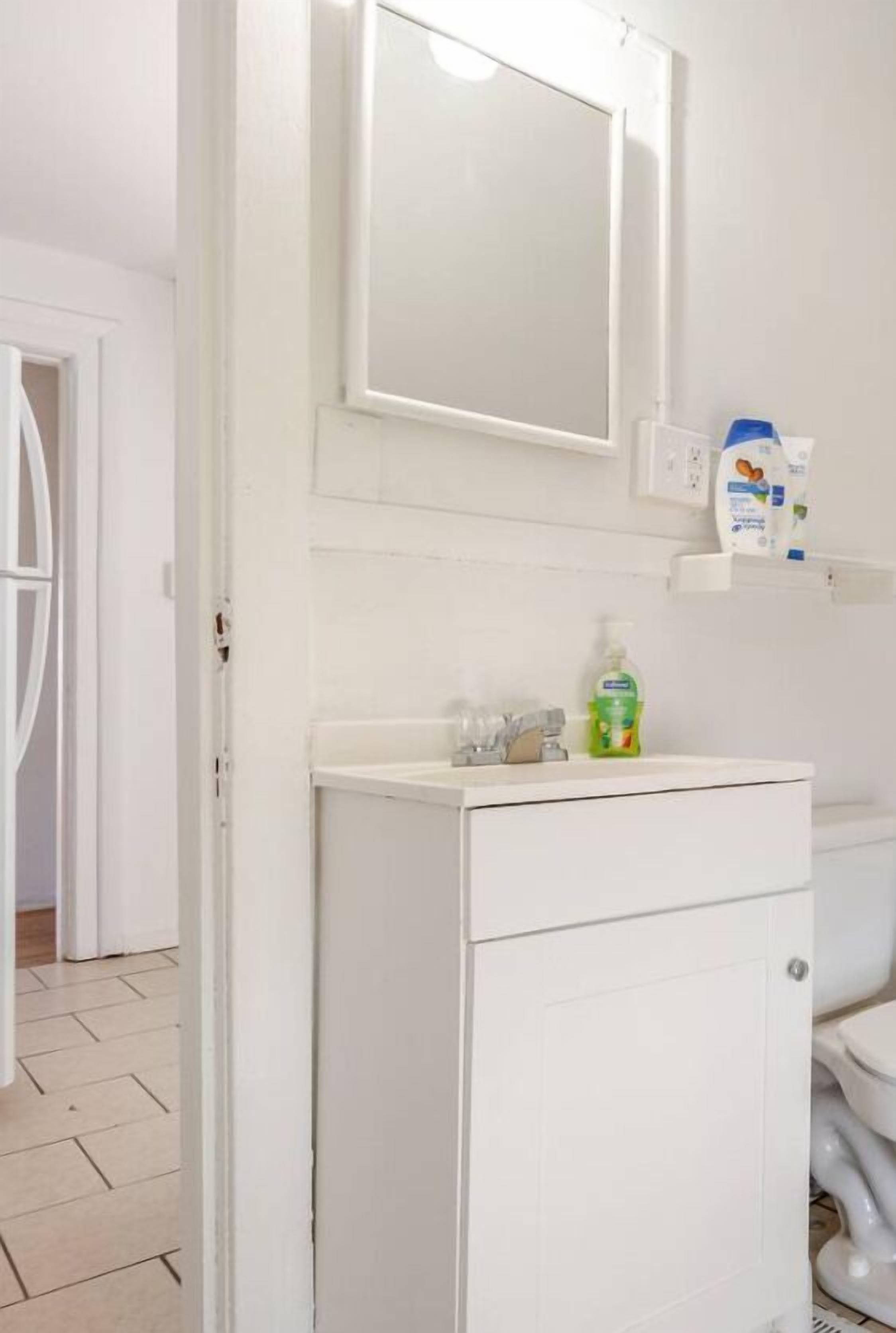 A bathroom with a white sink, mirror, and toilet. There is a shelf with toiletries.