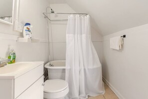 Une petite salle de bain blanche, équipée de toilettes, d’un lavabo et d’une douche.