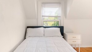 A bedroom with a bed, white walls, a window with blinds, and a nightstand with drawers. - Cozy Apartment in Ypsi with Wi-Fi (Ypsilanti)