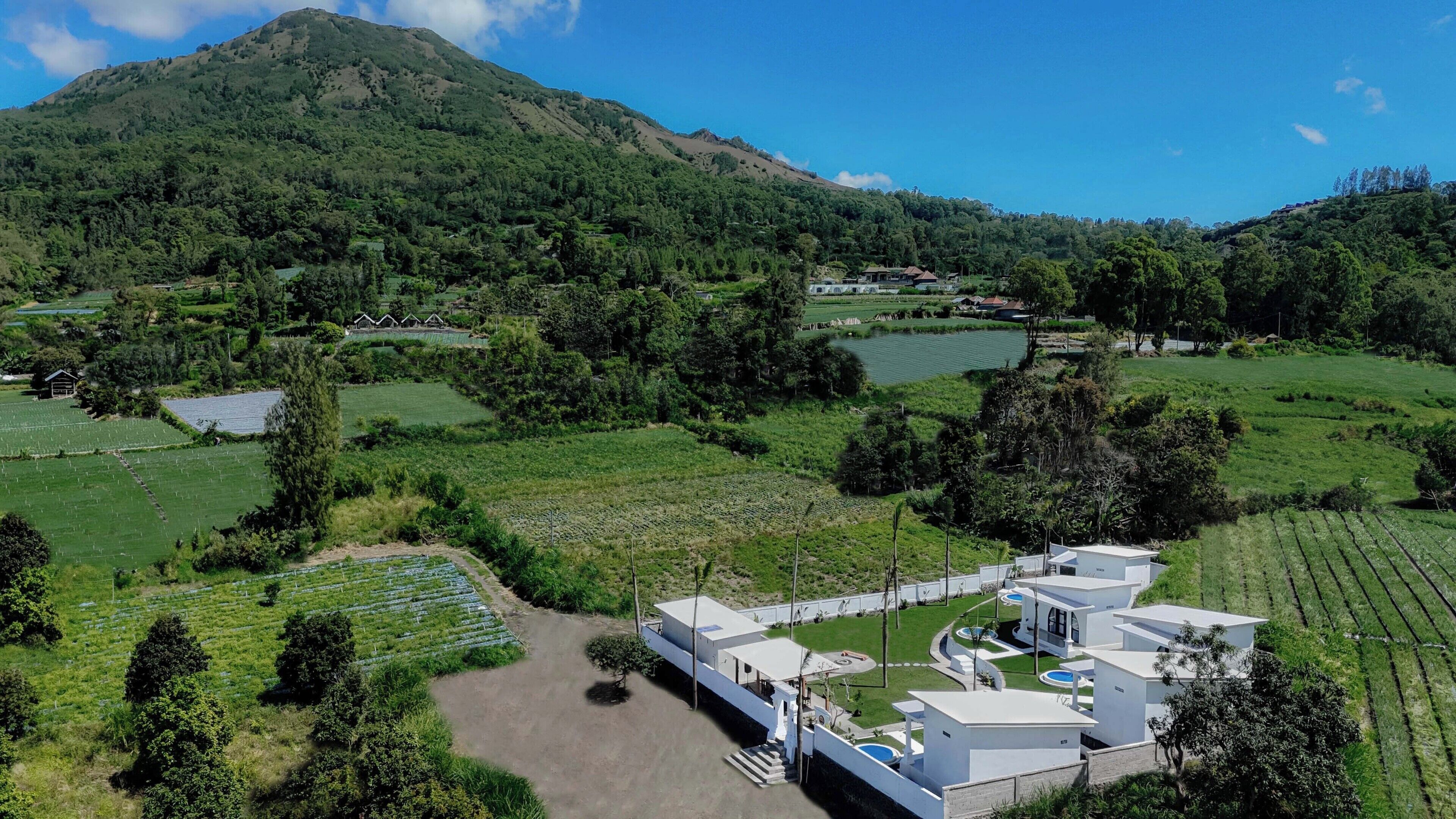 A modern hotel with a pool, surrounded by lush green fields and a mountain in the background.