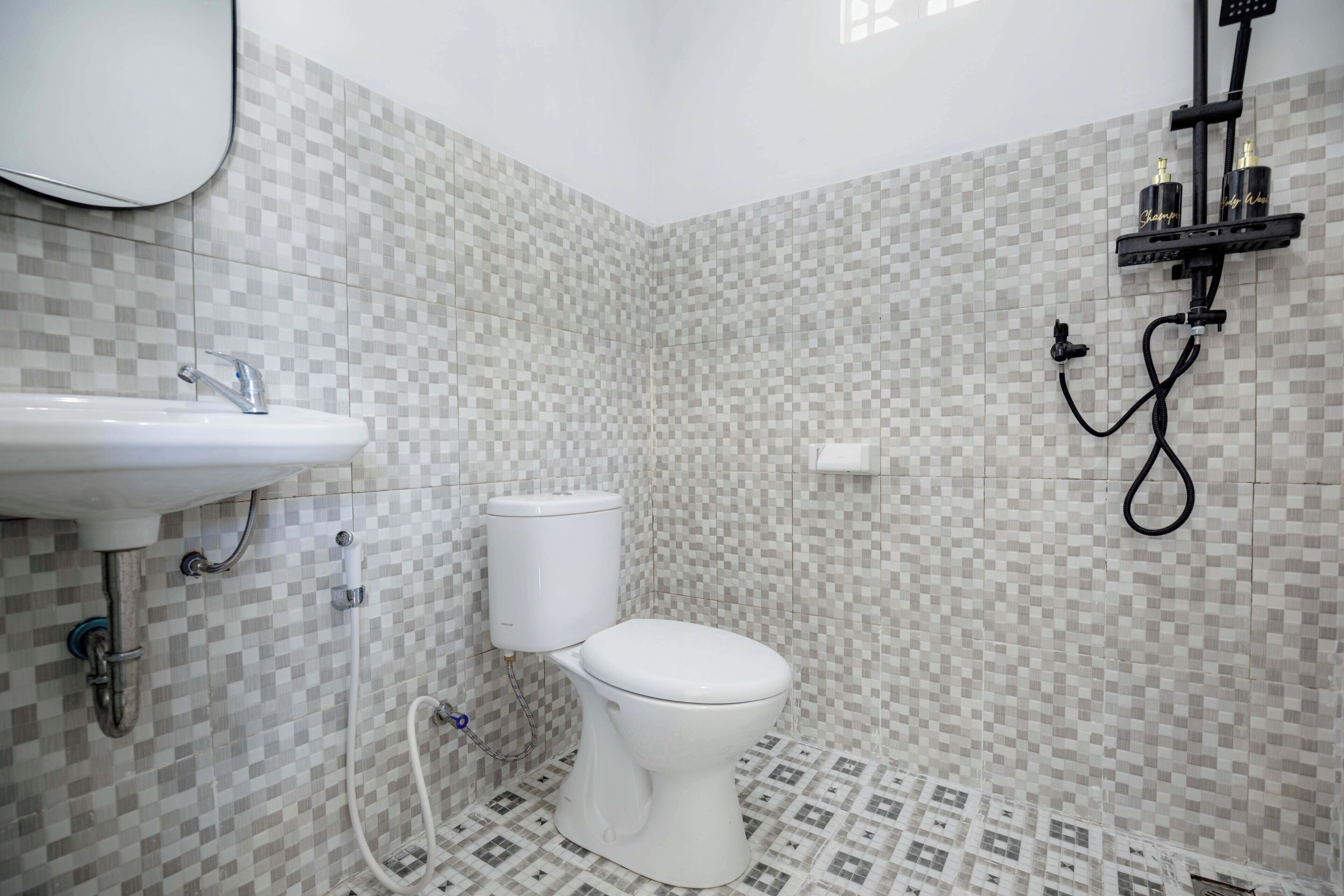 Une salle de bain avec un lavabo, des toilettes et une douche, le tout de couleur blanche. Les murs sont recouverts de carreaux disposés en motif à carreaux.