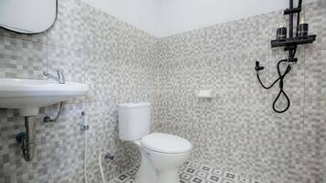 Une salle de bain avec un lavabo, des toilettes et une douche, le tout de couleur blanche. Les murs sont recouverts de carreaux disposés en motif à carreaux.