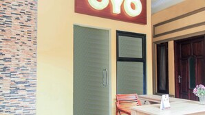 Una habitación de hotel con un cartel que dice 'OYO' sobre una puerta, una pequeña mesa con una silla y un jarrón con flores sobre la mesa.