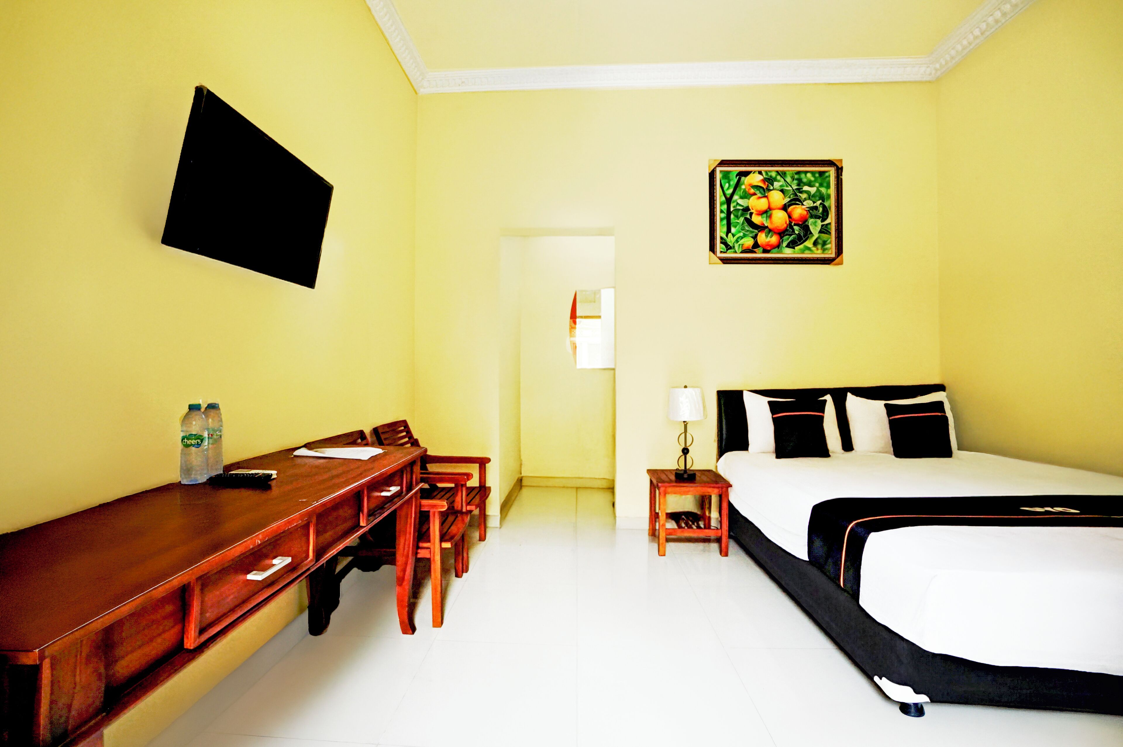 Quarto de hotel com cama, escrivaninha com cadeiras, televisão e um quadro na parede.