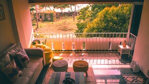 A cozy living room with a sofa, coffee table, and a view of a garden through a balcony railing. - Pine Beach House (Alappuzha)