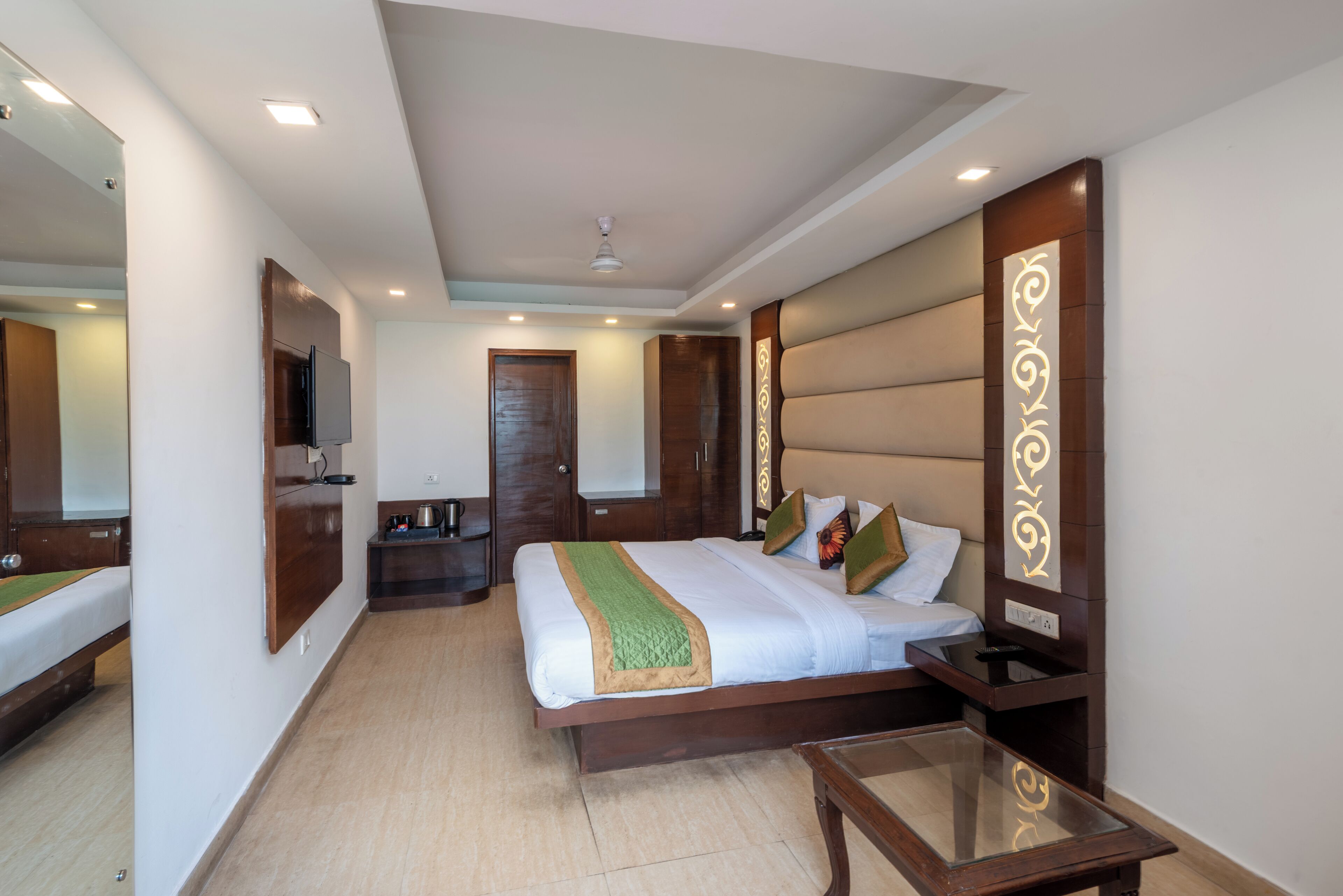 A hotel room with a bed, bedside table, a mirror, a small desk, and a wardrobe.