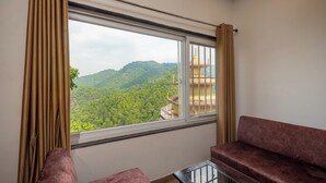 Ein Zimmer mit großem Fenster, das Blick auf eine bewaldete Gegend und ein Gebäude mit goldenem Dach gewährt. Es gibt zwei gepolsterte Sitzbereiche.