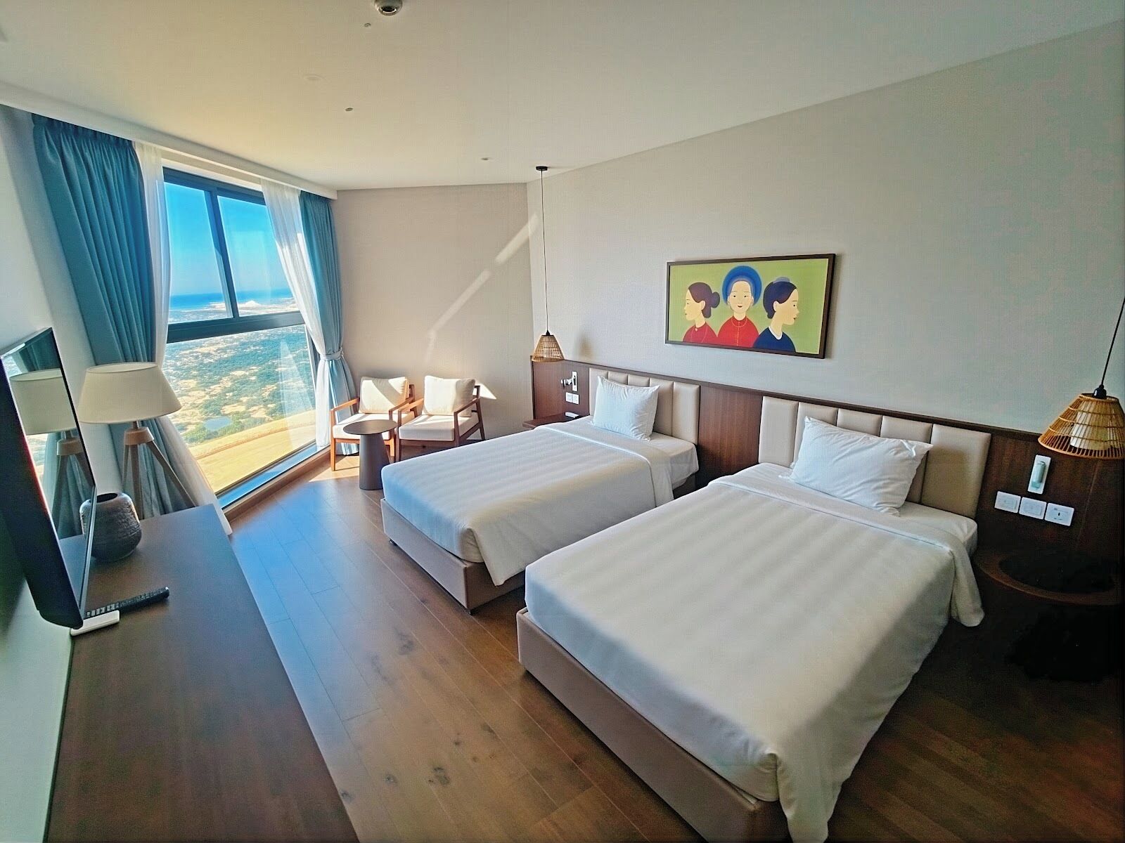 A hotel room with two beds, a desk, a chair, a lamp, and a painting on the wall.
