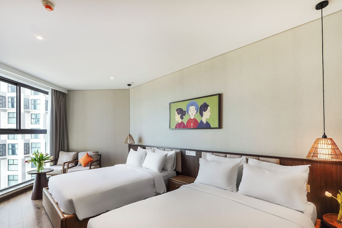 Une chambre d’hôtel avec deux lits, une petite table sur laquelle se trouve un vase, une chaise, un tableau accroché au mur et une vue sur les bâtiments par la fenêtre.