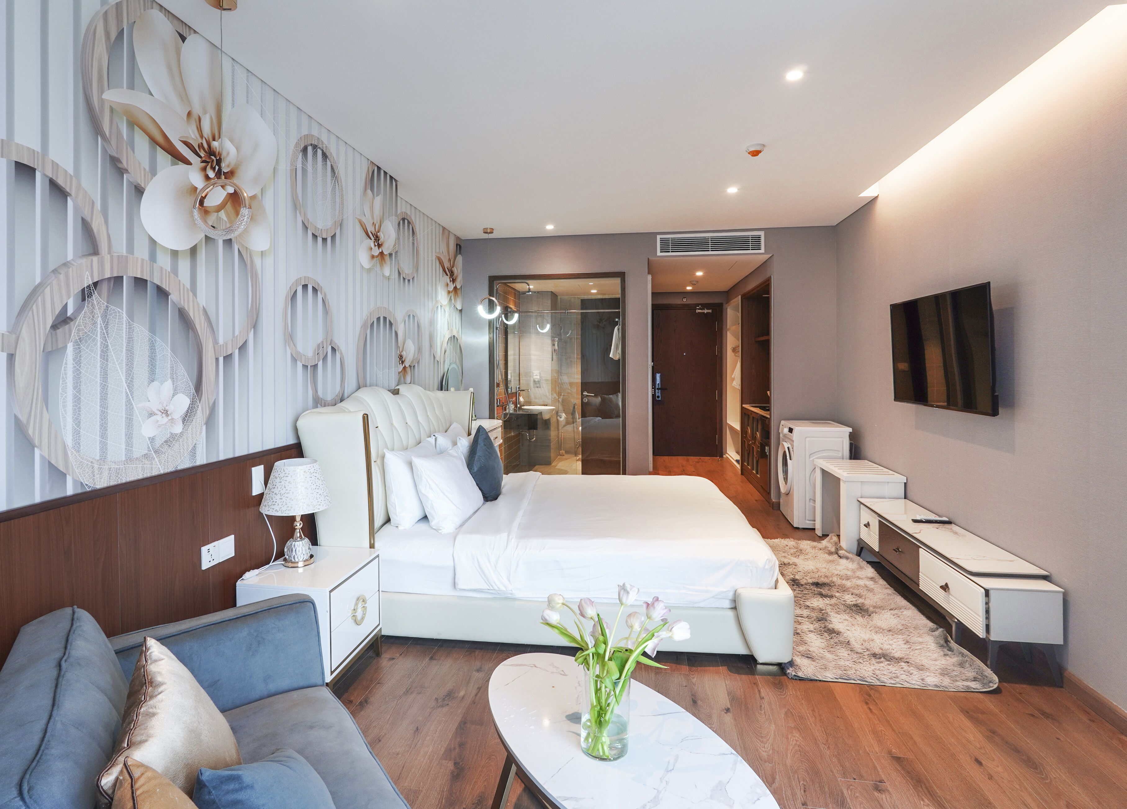 Un dormitorio moderno con una cama grande, una zona de estar con sofá, televisión y un baño con ducha y espejo.