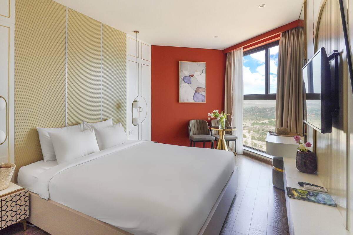 Une chambre d’hôtel avec un grand lit, un bureau avec une chaise, une fenêtre donnant sur un beau paysage et une télévision.