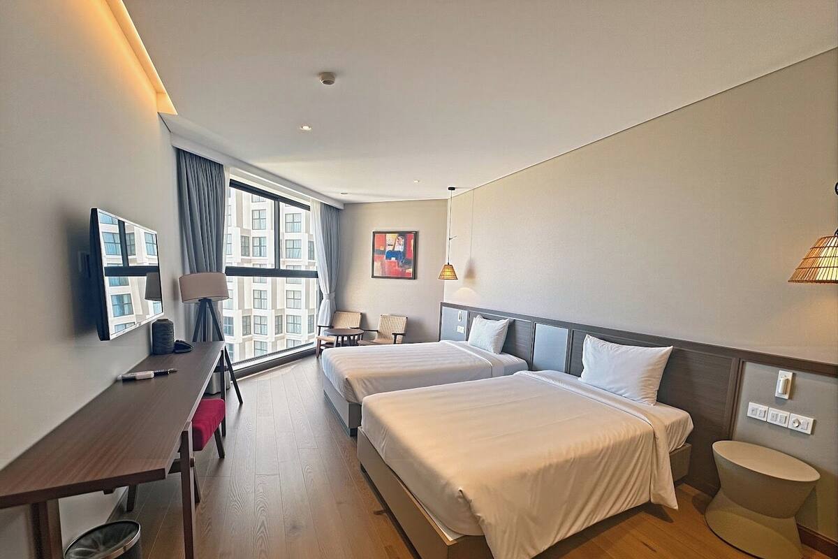 Une chambre d’hôtel avec deux lits, un bureau avec une chaise, une télévision et une fenêtre avec des rideaux.