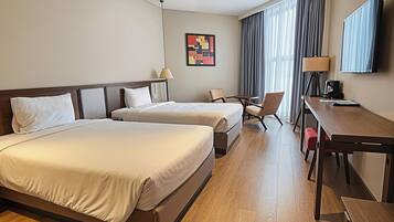 A hotel room with two beds, a desk, a chair, a TV, and a painting on the wall.