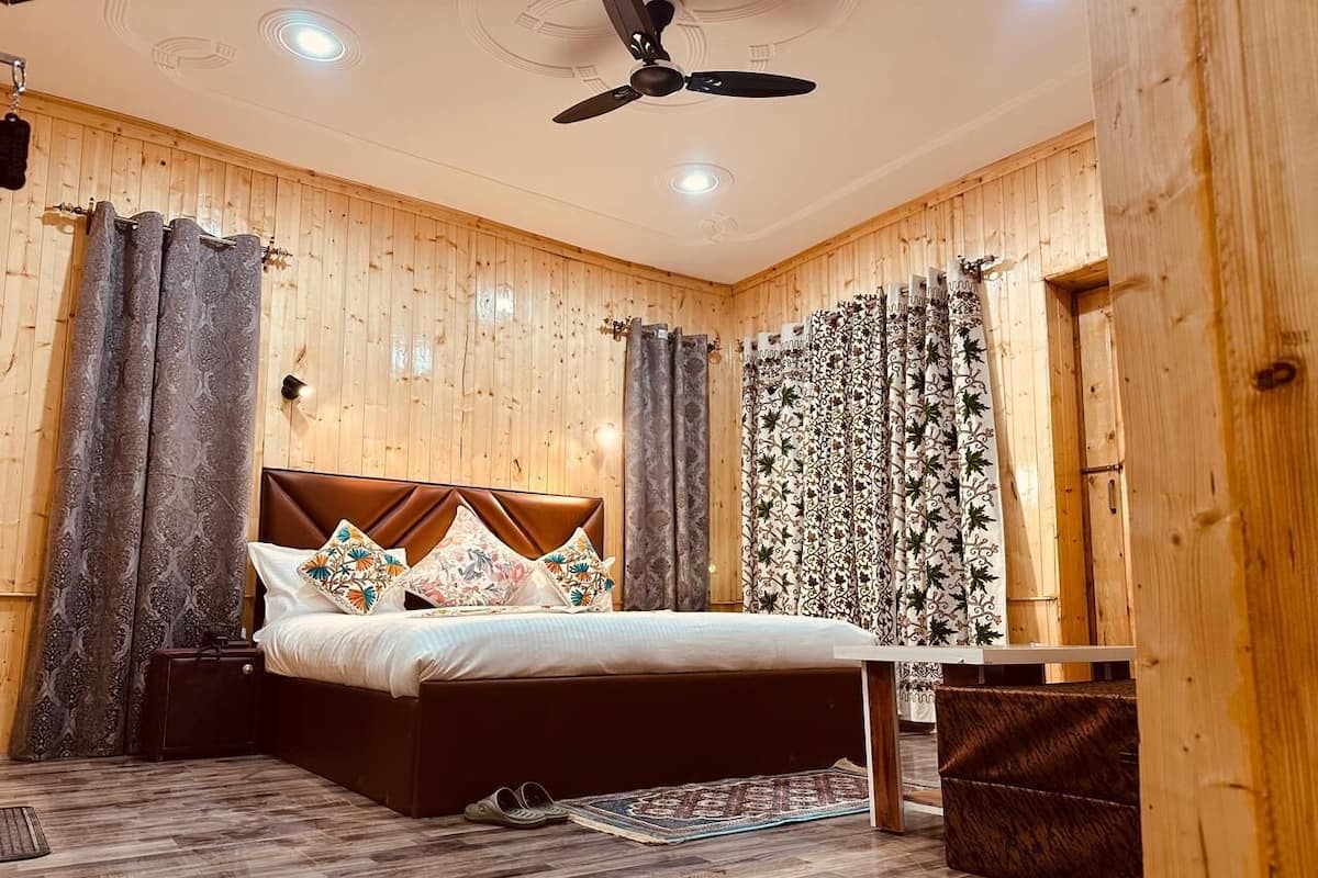 A wooden-paneled bedroom with a bed, curtains, a ceiling fan, and a small table.