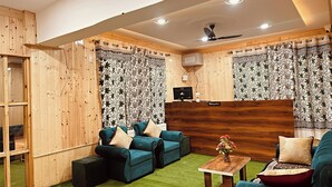 A room with wooden panel walls, two sofas with cushions, a small table with a vase, and a ceiling fan. - The Routes Pahalgam (Pahalgam)
