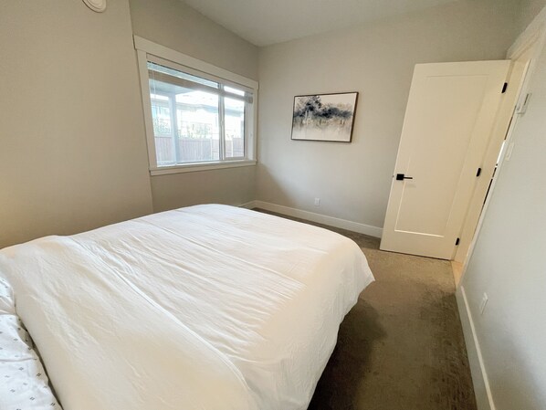 Un dormitorio con cama, ventana, puerta y un cuadro en la pared.