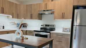 A modern kitchen with wooden cabinets, a stainless steel refrigerator, an oven, and a toaster. - Victoria luxury one bedroom suite (Langford)