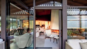 A modern interior with a glass partition, a fireplace, and a seating area with sofas and chairs. - AMONTI Chalets (Campo Tures)