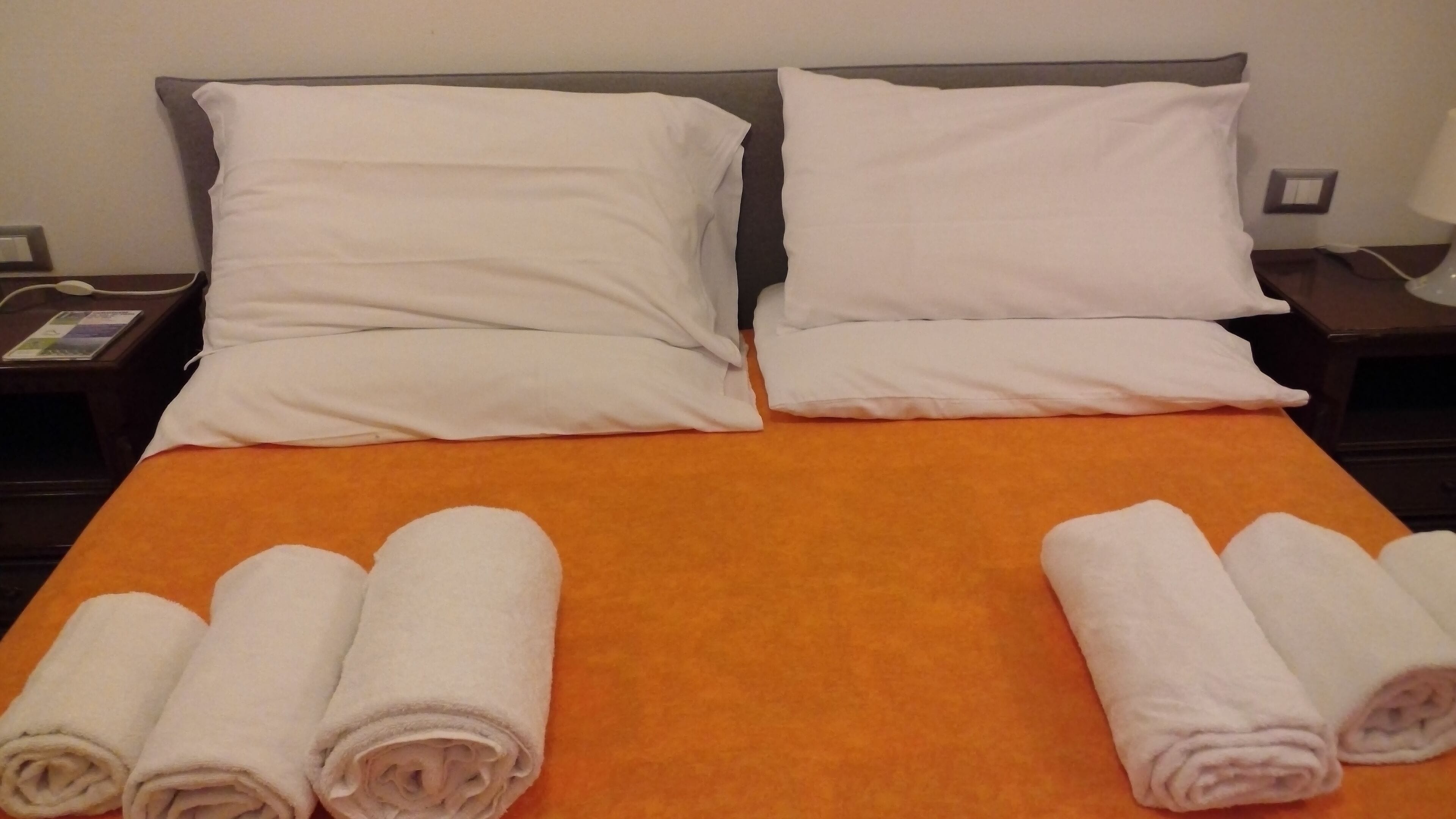 A hotel room with a large bed, two white pillows, and two rolled towels on the bed.