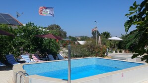 A rectangular swimming pool with a tiled edge, surrounded by lounge chairs and umbrellas. - Cozy countryhouse  with garden in the shadow of grapevine in a finca with pool (Gibraleón)