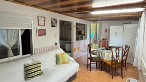 A cozy room with a bed, a dining table with chairs, a refrigerator, and a window with curtains. - Cozy countryhouse  with garden in the shadow of grapevine in a finca with pool (Gibraleón)