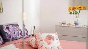 Un lit bien fait, agrémenté de coussins à motifs floraux, un vase avec des tournesols et une commode ornée d’objets décoratifs.