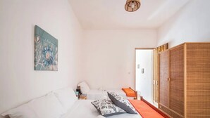 Une chambre à coucher avec un lit, des oreillers, une serviette enroulée, une table de chevet, une lampe, un tableau et une armoire.