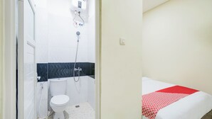 Et badeværelse med toilet, bruser og en seng med et rødt og hvidt sengetæppe.