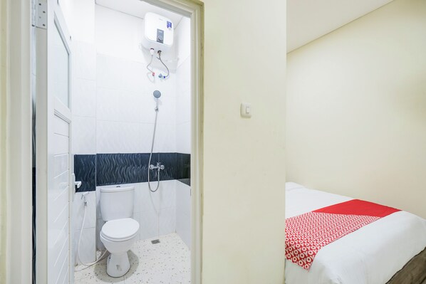 A bathroom with a toilet, shower, and a bed with a red and white bedspread.