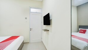 Et hotelværelse med en seng, et fjernsyn ophængt på væggen og en dør.