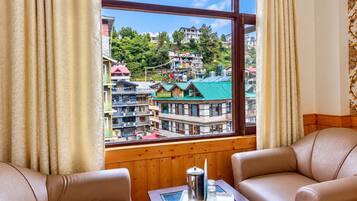 A room with two leather sofas, a wooden table with a coffee pot and glasses, and a window with a view of a town with colorful buildings.