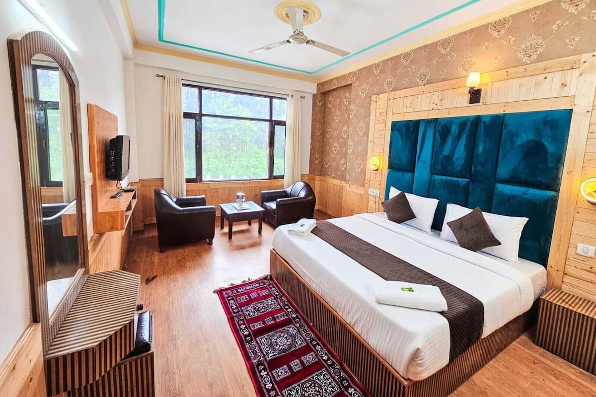 Habitación de hotel con una cama grande, un escritorio con silla, televisor y ventana con cortinas.