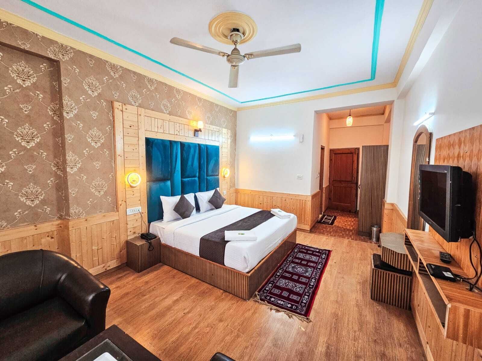 A hotel room with a wooden headboard, a bed with white linens, a black leather chair, a TV, and a ceiling fan.