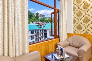 Ein Hotelzimmer mit einer Wandpaneelaus Holz, einem Fenster mit Vorhängen, einem Sofa, einem kleinen Tisch mit Kaffeemaschine und einer Zeitschrift sowie einem gemusterten Wandpapier.