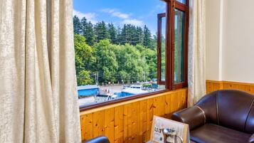 A room with a view of a forest and a road, a wooden wall, a leather sofa, and a table with a menu and a coffee pot.