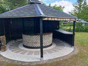A covered outdoor barbecue area with a circular brick fire pit, a wooden sign reading 'BALHUSE INN,' and a surrounding gravel path.